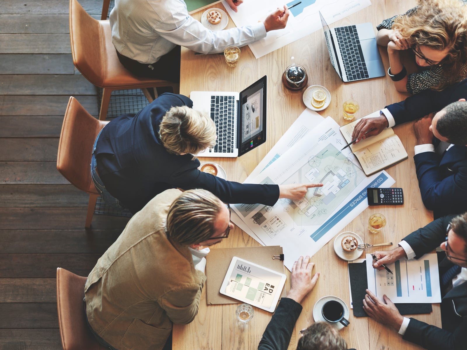 Vue de dessus d'une table de réunion, plusieurs personnes travaillant sur des documents et des ordinateurs