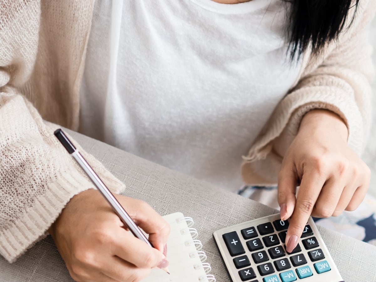 Une personne note ses chiffres sur un carnet, calculatrice à portée de main