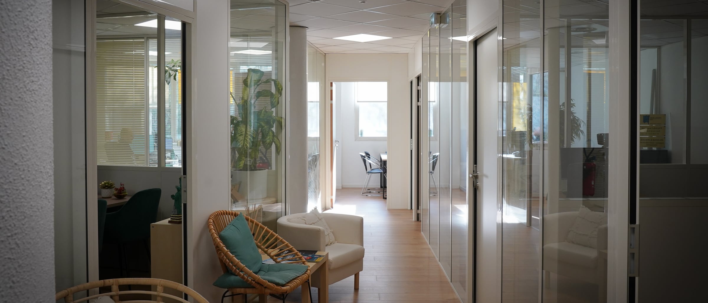 Couloir de bureaux à cloisons vitrées et salle d'attente avec fauteuils, dans les locaux de Nanadresse
